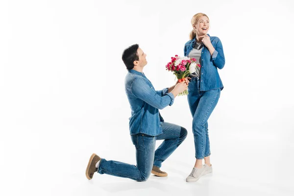 Чоловік стоїть на одному коліні і дарує щасливій жінці букет квітів ізольований на білому — стокове фото