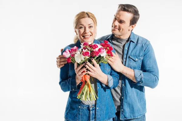 Усміхнений чоловік приймає жінку з весняними квітами ізольовано на білому — стокове фото