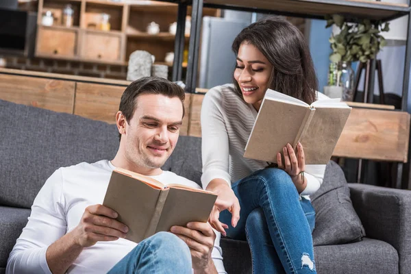 Glückliches multiethnisches Paar, das zu Hause gemeinsam Bücher liest — Stockfoto