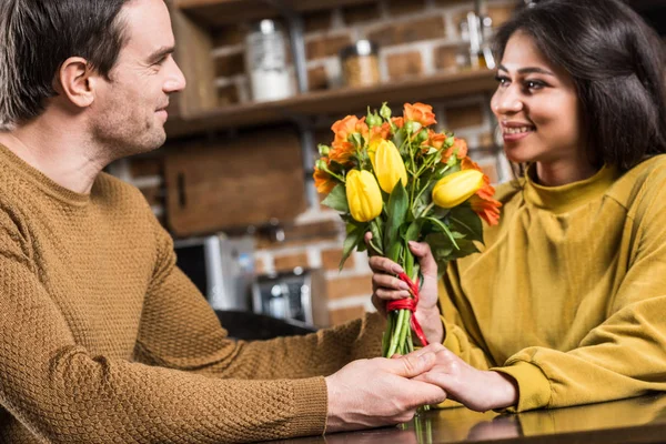 Jovem sorridente apresentando lindo buquê de flores para namorada feliz em casa — Fotografia de Stock