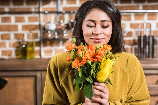 Hermosa mujer joven feliz con los ojos cerrados sosteniendo ramo de flores en casa - foto de stock