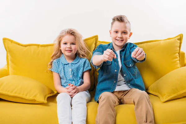 Kleine Fahrerin sitzt mit Schwester auf gelbem Sofa — Stockfoto
