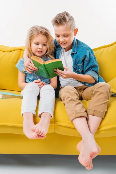 Frères et sœurs lisant le livre et assis sur un canapé jaune — Photo de stock