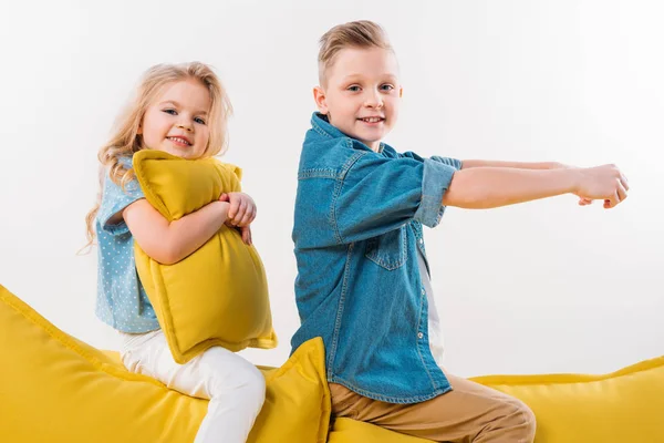 Feliz chico fingiendo ser un conductor mientras está sentado en el sofá amarillo con su hermana - foto de stock