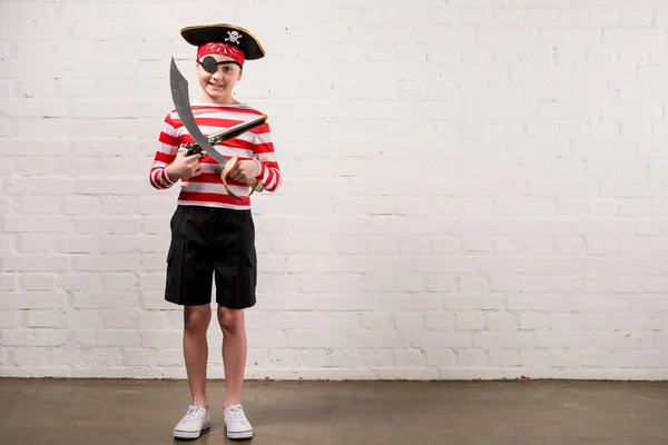 Pequeño niño sonriente con cuchillo de juguete y pistola en traje de pirata - foto de stock