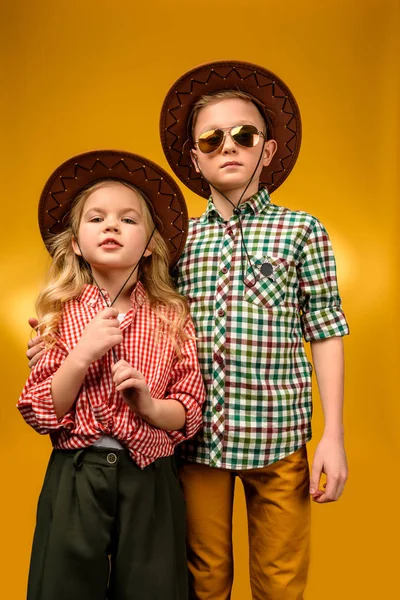 Kleiner stylischer Cowboy und Cowgirl posiert in Hüten, isoliert auf gelb — Stockfoto