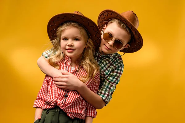 Pouco elegante cowboy e cowgirl em chapéus abraçando isolado no amarelo — Fotografia de Stock