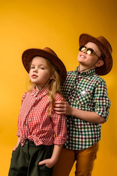 Pouco cowboy elegante e cowgirl em chapéus, isolado em amarelo — Fotografia de Stock