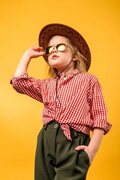 Hermosa vaquera con estilo en sombrero y gafas de sol, aislado en amarillo - foto de stock