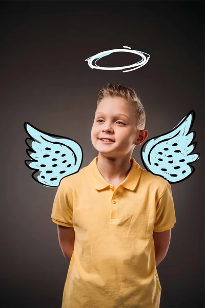 Retrato de adorable niño preadolescente con alas dibujadas y nimbo como ángel, aislado en gris - foto de stock