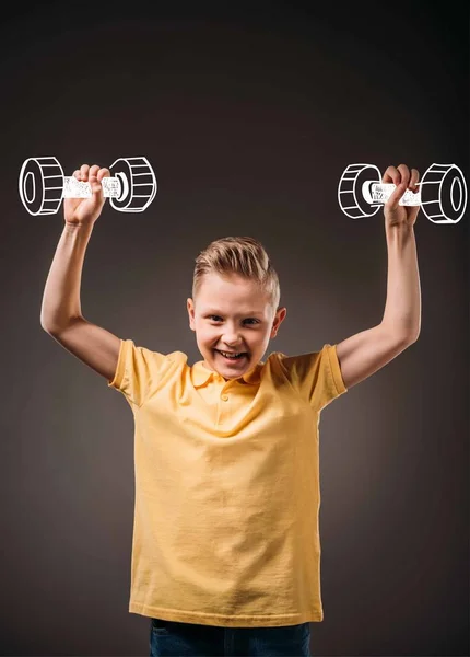 Улыбающийся мальчик, притворяющийся спортсменом и тренирующийся с гантелями, изолированный на сером — стоковое фото