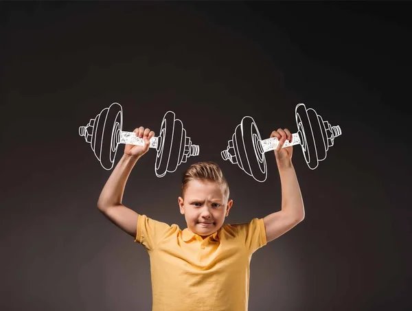 Preteen boy pretending to be a sportsman and lifting big drawn dumbbells, isolated on grey — Stock Photo