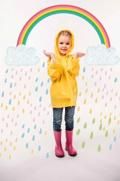 Little kid in yellow raincoat and rubber boots, with rainy clouds and colorful rainbow illustration — Stock Photo