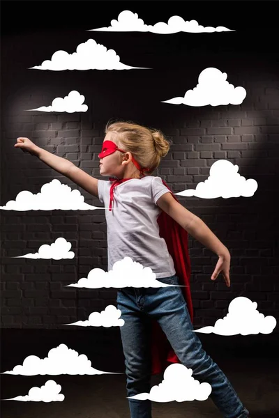 Девочка летит в красной маске супергероя и летит в облаках — стоковое фото