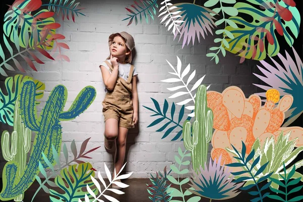 Pensive child in safari costume standing at white wall with cactuses illustration — Stock Photo
