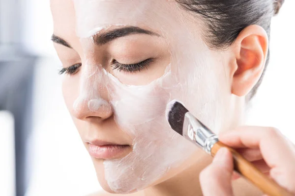 Cropped image of beautician applying cream on girl face isolated on white — Stock Photo