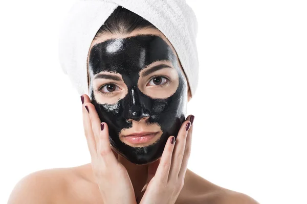 Hermosa chica en cosmética máscara facial de arcilla negra mirando a la cámara aislada en blanco - foto de stock