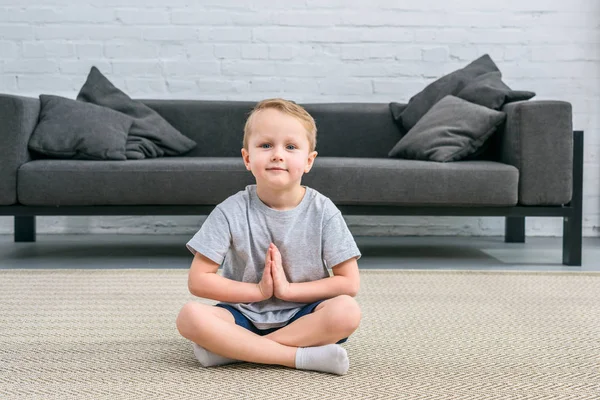 Petit garçon pratiquant le yoga en position lotus dans le salon — Photo de stock