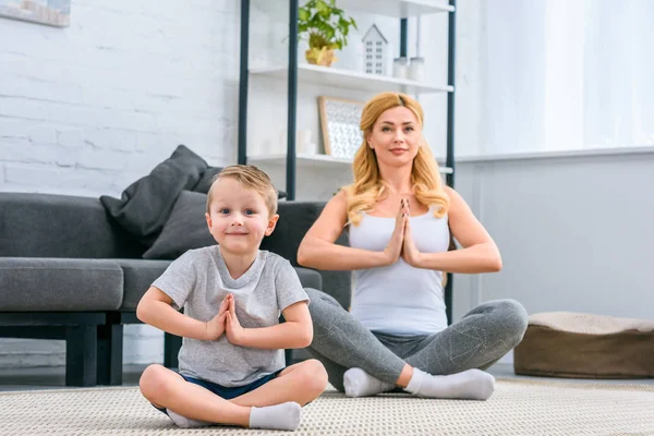 Mãe com filho pequeno praticando ioga na posição de lótus na sala de estar — Fotografia de Stock