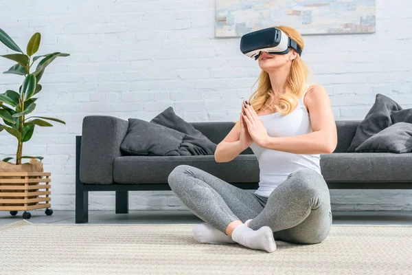 Mujer joven practicando yoga en posición de loto y usando auriculares de realidad virtual - foto de stock