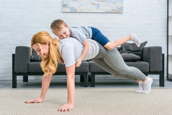 Smiling mother doing plank with little boy on back — Stock Photo
