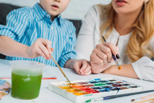 Imagen recortada de la madre y el hijo sumergiendo pinceles en pinturas - foto de stock