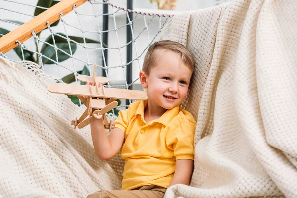 Smiling boy playing with wooden airplane toy in hammock — Stock Photo