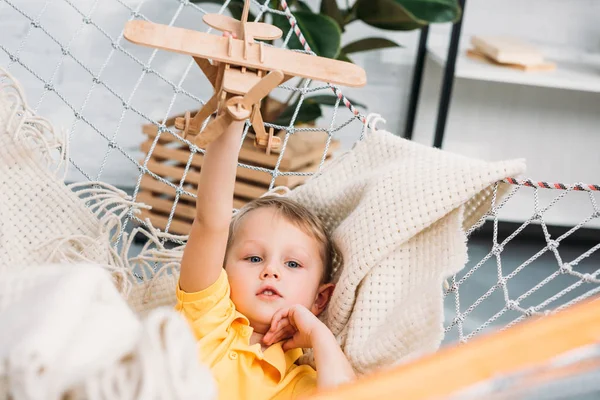 Menino feliz brincando com brinquedo de avião de madeira na rede — Fotografia de Stock