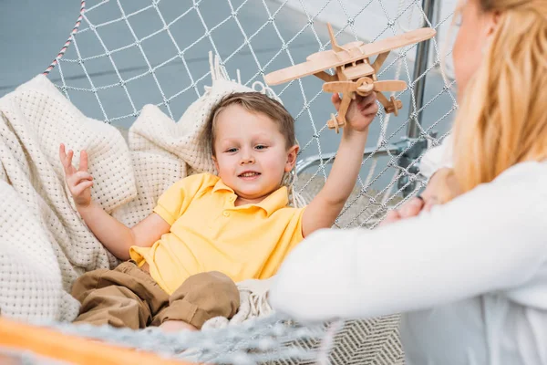 Abgeschnittenes Bild von Frau und kleinem Jungen beim Spielen mit hölzernem Flugzeugspielzeug in der Hängematte — Stockfoto