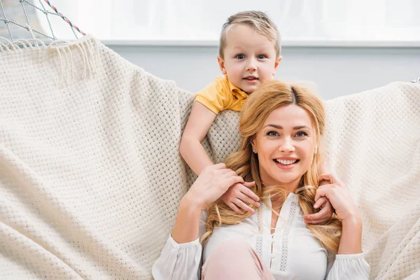 Piccolo ragazzo abbracciare sorridente madre mentre lei posa in amaca — Foto stock