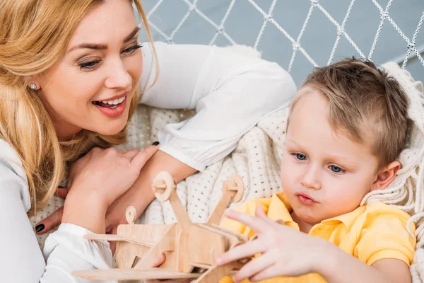 Sorrindo mãe assistindo filho brincando com brinquedo de avião de madeira — Fotografia de Stock