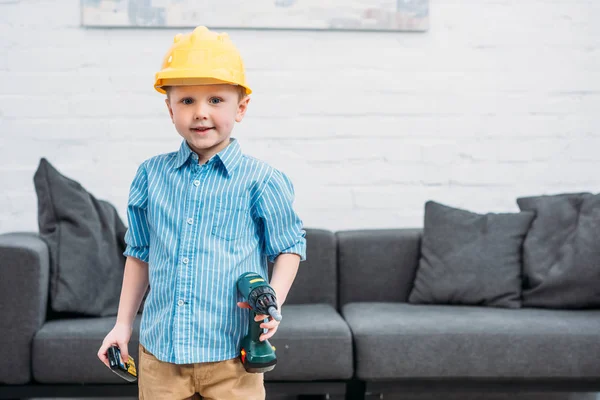 Kleiner Junge mit Schutzhelm und Spielzeugbohrer gibt sich als Arbeiter aus — Stockfoto