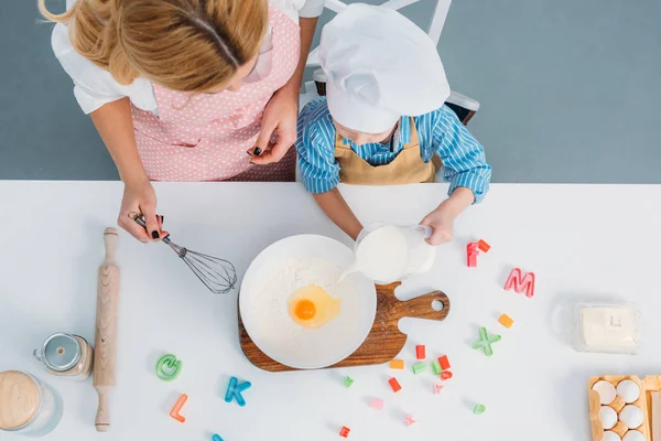 Top view of mother and boy pouring milk into bowl with egg and flour — Stock Photo