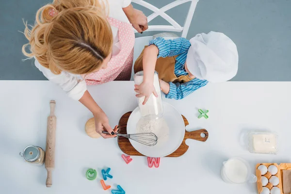 Top view of mother and boy pouring milk into bowl with egg and flour — Stock Photo