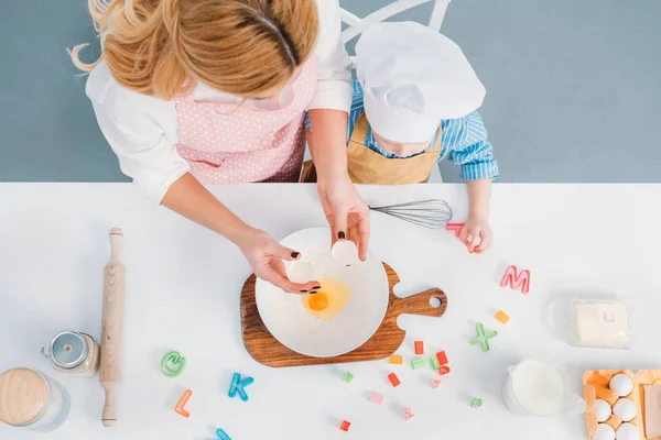 Vista superior de mãe e filho derramando ovo em tigela com farinha — Fotografia de Stock