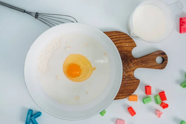 Top view of bowl with egg and flour at table with kitchenware and milk — Stock Photo