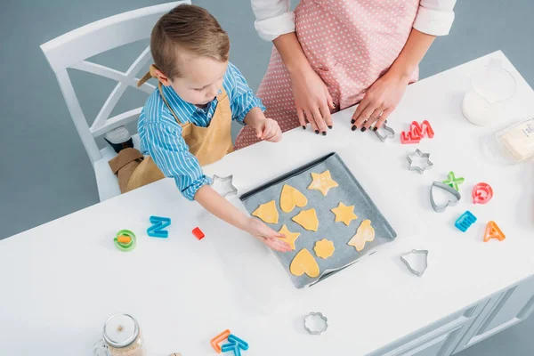 High angle view of mother and son putting tough for cookies on baking sheet — Stock Photo