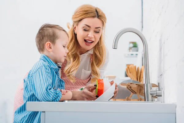 Hijo y madre lavando cuenco en la cocina - foto de stock