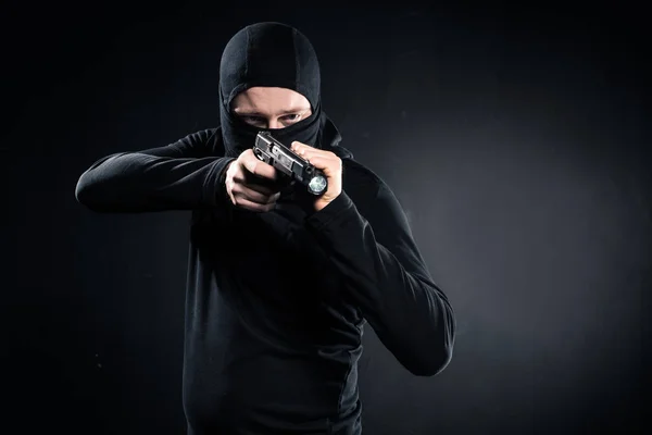 Ladrão em balaclava apontando com arma em preto — Fotografia de Stock