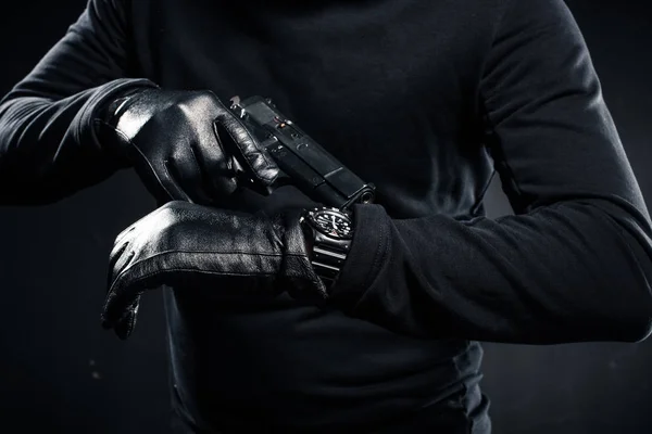Man in gloves with gun checking his watch — Stock Photo