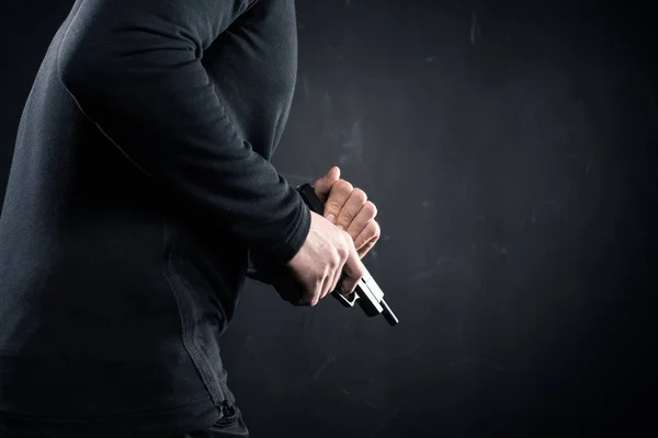 Robber in black closes holding gun in hands — Stock Photo