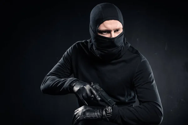Hombre criminal en guantes con pistola revisando su reloj - foto de stock