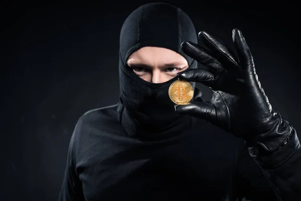 Hombre de pasamontañas negro sosteniendo bitcoin dorado - foto de stock
