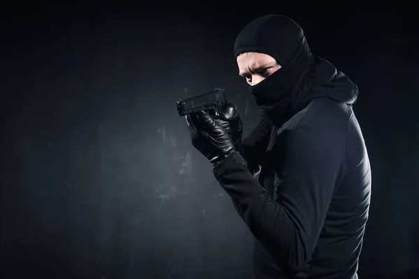 Male criminal in balaclava and gloves aiming with gun on black — Stock Photo