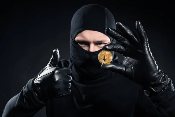 Homem de balaclava preto segurando bitcoin e mostrando o polegar para cima — Fotografia de Stock