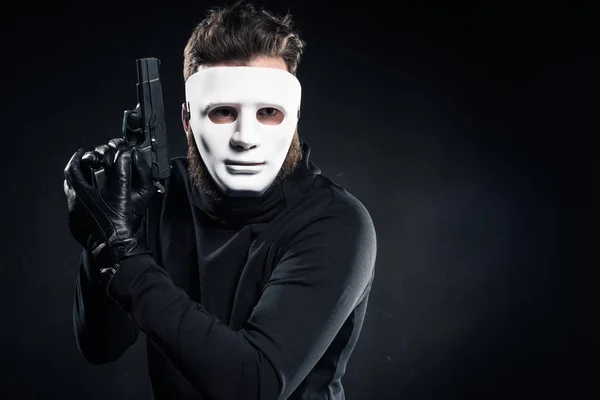 Verbrecher in weißer Maske und schwarzer Kleidung mit Waffe — Stockfoto