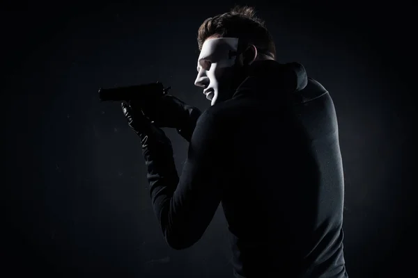 Robber in mask and gloves aiming with gun on black — Stock Photo
