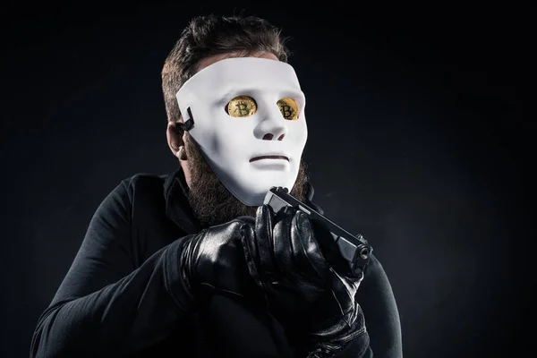 Male criminal in mask and bitcoins on eyes aiming with gun — Stock Photo