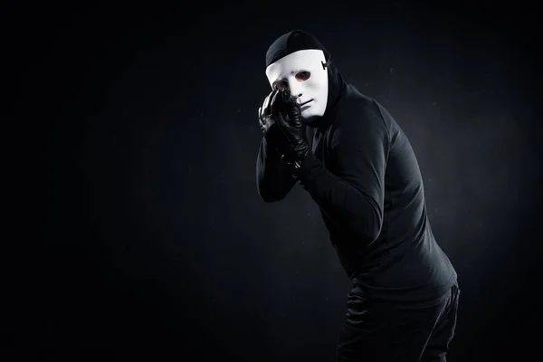 Male robber in mask aiming with gun on black — Stock Photo