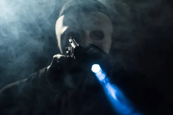 Criminal in mask and balaclava aiming with gun and flashlight — Stock Photo